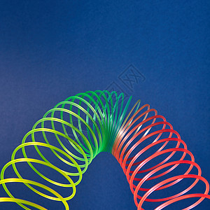 灵活的彩虹塑料弹簧,以抛物线的形式出现蓝色背景上,并文字的位置几何抛物线来自彩色的细长玩具图片
