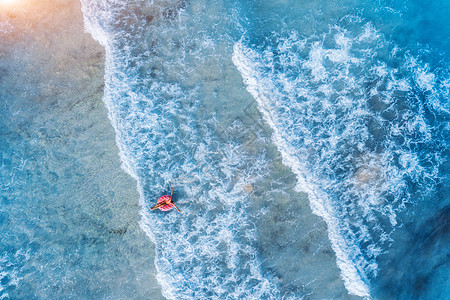 鸟瞰年轻的女人游泳与粉红色甜甜圈游泳环清澈的蓝色海洋与美丽的波浪日落夏天热带航空景观图片