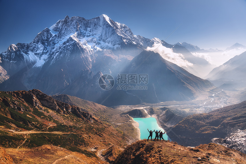 快乐的人举手臂山峰上抗美丽的湖泊,日出时雪山风景与男人女人,岩石云,蓝天与阳光尼泊尔旅行徒步旅行图片