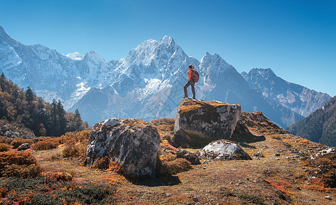 站着的女人,背着背包石头美丽的山日落风景与运动女孩,高岩石,雪峰,蓝天秋天尼泊尔旅行生活方式喜马拉雅图片