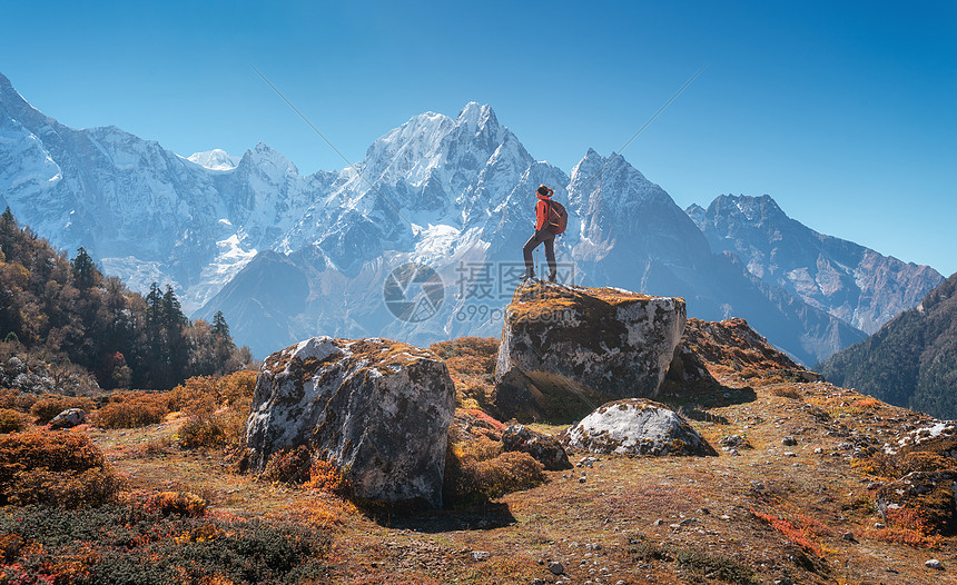站着的女人,背着背包石头美丽的山日落风景与运动女孩,高岩石,雪峰,蓝天秋天尼泊尔旅行生活方式喜马拉雅图片