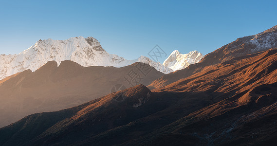 美丽的山脉雪峰阳光明媚的早晨尼泊尔日出时喜马拉雅山脉的轮廓五颜六色的景观,高岩石,蓝天金色的阳光神奇的喜马拉图片