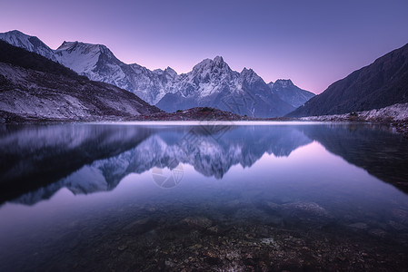 黄昏山湖山湖日出时完美的倒影美丽的风景与紫色的天空,雪山,山丘,雾湖黄昏尼泊尔雪覆盖的岩石反射水中背景