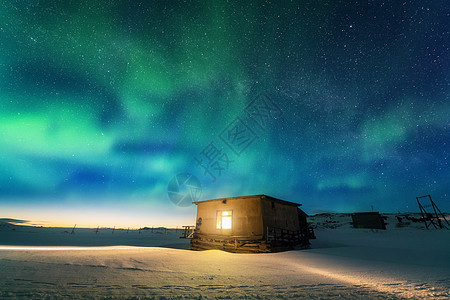 北极光覆盖着古老的小房子,窗户发出光俄罗斯泰伯卡的北极光蓝天上星星绿色的北极光夜间冬季景观与极光,建筑图片