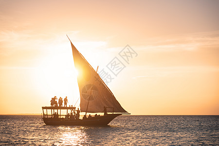 夏天日落时海洋中的帆船热带景观与船中人的轮廓,橙色的天空与金色的阳光晚上游艇水上非洲桑给巴尔旅行假期图片