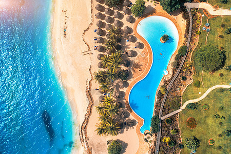 鸟瞰游泳池,雨伞,沙滩,绿树蓝海夏季日落时印度洋海岸的风景景观与蔚蓝的水,阳伞,棕榈树豪华度假村自然图片