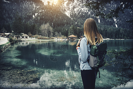 带着背包的轻女人秋天的日落时站湖边意大利旅行风景与苗条的女孩,倒影水,雪岩,绿树秋天古董图片