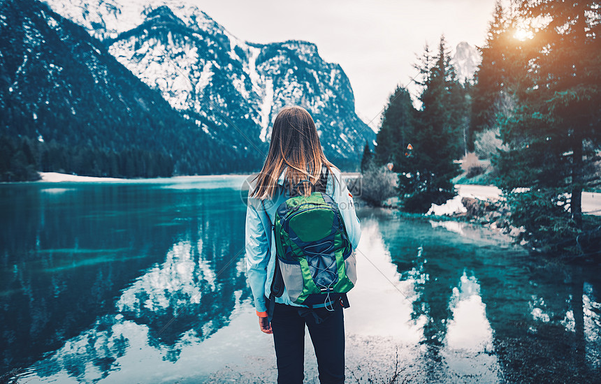 轻的女人带着背包站山湖的海岸上,秋天的日落时,意大利旅行风景与苗条的女孩,倒影水,雪岩,绿树复古色调图片