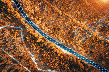 日落时美丽的秋林中的道路鸟瞰完美的沥青道路的顶部景观,秋天橙色叶子的树木五颜六色的景观与公路穿过林地旅行日落时图片