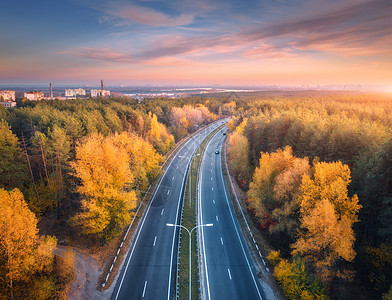 日落时美丽的秋林中的道路鸟瞰五颜六色的风景与空的公路,树木与绿色橙色的叶子,粉红色的天空与云彩秋天巷道的顶部视图图片