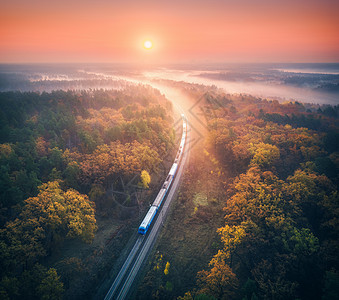 秋天日出时,美丽的森林里乘火车秋季通勤列车的鸟瞰图五颜六色的景观与铁路,雾树,橙色的叶子,红色的天空薄雾的风图片