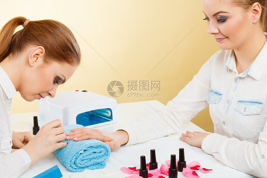 美甲工艺美容院的轻美容师女顾客女客户手握桌上的指甲油 毛巾文件照明仪器专业美甲师绘画女指甲高清图片下载 正版图片 摄图网