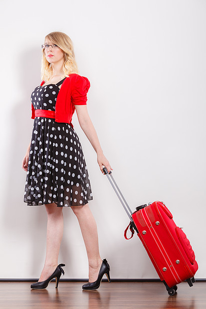 旅行度假的优雅的轻女子,穿着波尔卡圆点黑色连衣裙,高跟鞋,红色手提箱,为旅行好准备优雅的时尚女人带着红色的手提箱图片