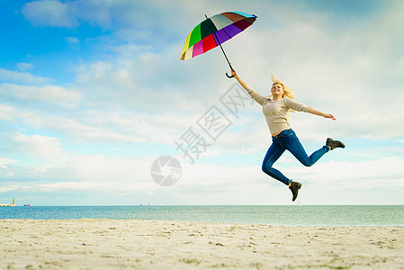 快乐,享受天气,感觉很棒的女人海边的海滩上用五颜六色的雨伞跳跃,阳光明媚的日子晴朗的蓝天女人海滩上着五颜六色图片