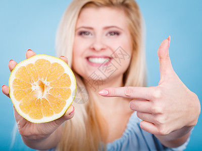 女人微笑的女孩手里着半的绿色黄色葡萄柚柑橘类水果,用手指指着,推荐健康的饮食,蓝色上减肥女人指着葡萄柚柑橘类水果图片
