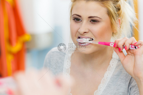 女人刷牙特写浴室里带牙刷的金发女孩,看着镜子口腔卫生女人浴室刷牙图片