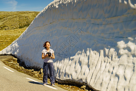 游客妇女与相机拍摄旅游照片高雪墙挪威的山路极光,夏季时间游客与相机高雪墙道路,挪威图片