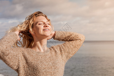 穿着毛衣,阳光下风着头发,快乐的女人户外穿毛衣图片