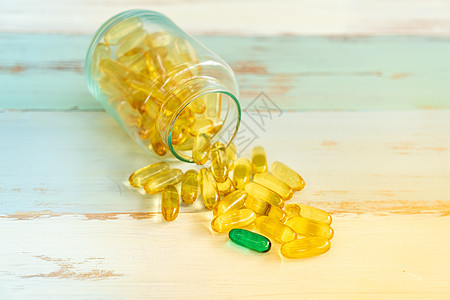 种绿色药丸药物黄色药丸中脱颖而出,并老式木制背景上药丸瓶中溢出图片