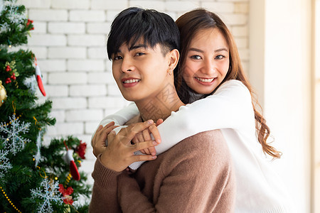 轻的亚洲成青少夫妇拥抱庆祝诞节,客厅与诞树装饰装饰图片