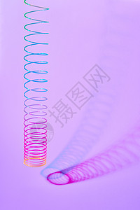 粉红色的薰衣草背景上用两个弯曲的阴影编彩色塑料螺旋玩具,放置文本彩虹塑料弹簧玩具,两个双调阴影图片