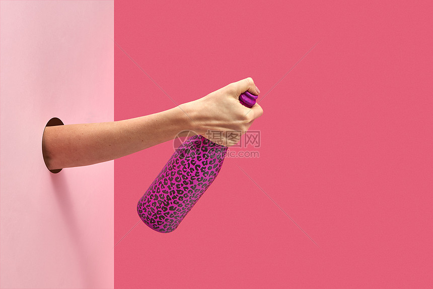 女手握着涂黑点的酒瓶,拇指墙壁上的洞,背景双粉红色的背景,柔的阴影,拇指握住酒瓶,涂上热粉色图片