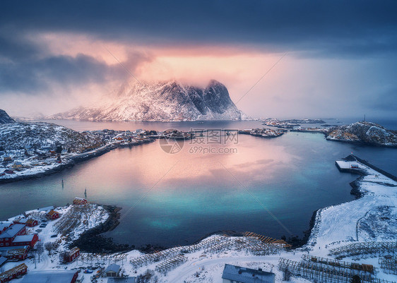 雪山的鸟瞰,海边的村庄,冬天日落时的橙色天空莱茵河,洛芬岛,挪威的顶级景观穆迪景观与高岩石,房屋,罗布,反射水中图片