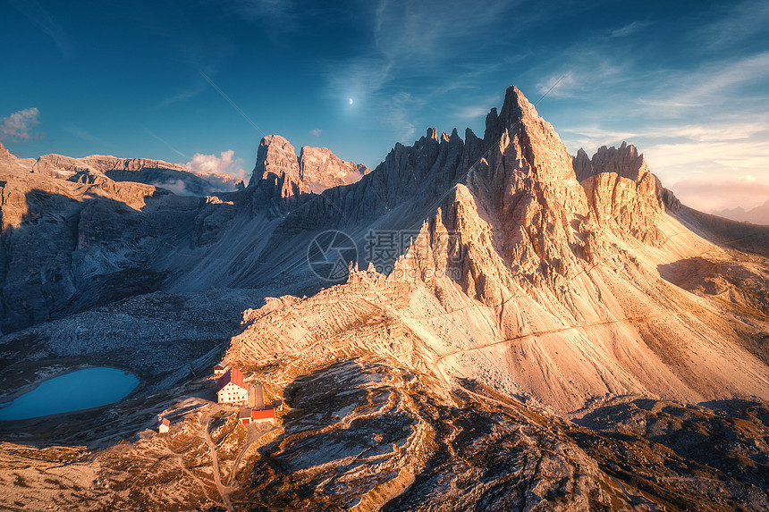 秋天日落时,山上美丽的房子教堂风景与建筑物,高岩石,湖泊蓝天与月亮云黄昏意大利白云石TreCime公园的鸟瞰图图片