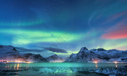 北极光海边,雪山城市灯光夜间挪威洛福滕岛的北极光极地灯光的星空冬季景观与极光反射水中图片