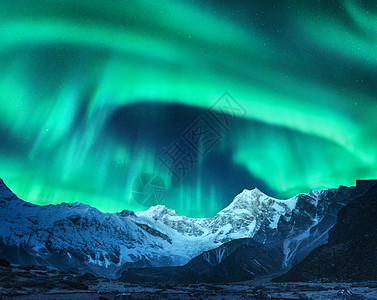 挪威雪覆盖山峰上方的北极光冬天的北极光夜间景观与绿色极地灯雪山星空,岩石上极光图片