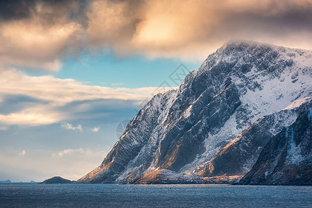 美丽的大雪覆盖了冬天日落时的群山挪威洛福腾群岛风景与雪岩,大海,蓝天与橙色的云晚上旅行自然图片