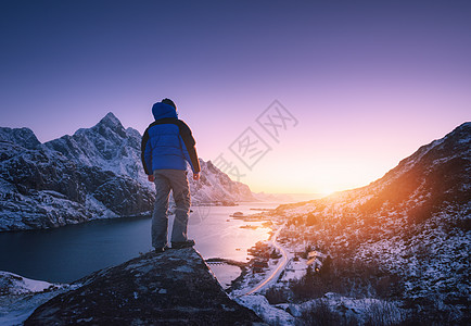 人站山顶上,迎着雪山,峡湾冬天五颜六色的日落轻的男人石头,海岸岩石,蓝色的天空洛福滕岛,挪威旅行徒步旅行图片