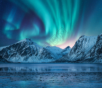 北极光覆盖雪山,海岸的湖泊倒影水中白雪覆盖的岩石上方的北极光冬季景观与极地灯,峡湾星空明亮的极光图片