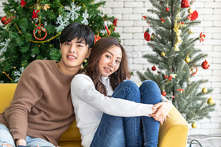 轻的亚洲成青少夫妇拥抱庆祝诞节客厅与诞树装饰图片