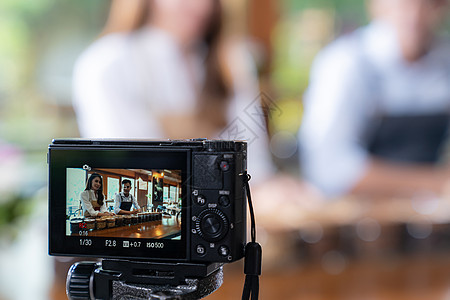 轻的亚洲业主企业家Vlog回顾咖啡馆咖啡店,并生活社交媒体上,咖啡馆用相机进行线营销用于启动小企业营销消费主义图片