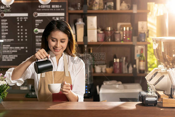 轻的亚洲女咖啡师咖啡馆里为顾客倒新鲜牛奶准备铁咖啡图片