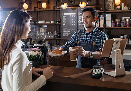 自助餐厅亚洲咖啡师的肖像,走咖啡牛角包杯,并咖啡馆与其他咖啡师后台工作背景
