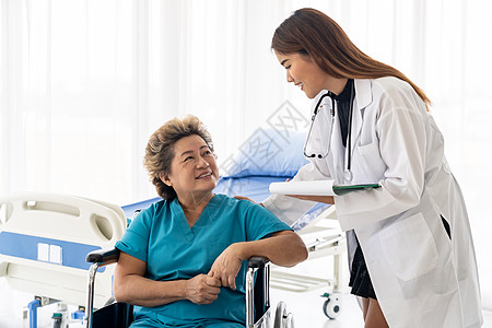 亚洲自信医生照顾者谈论健康问题与老妇女病人坐轮椅上的医院病房,而每天检查图片