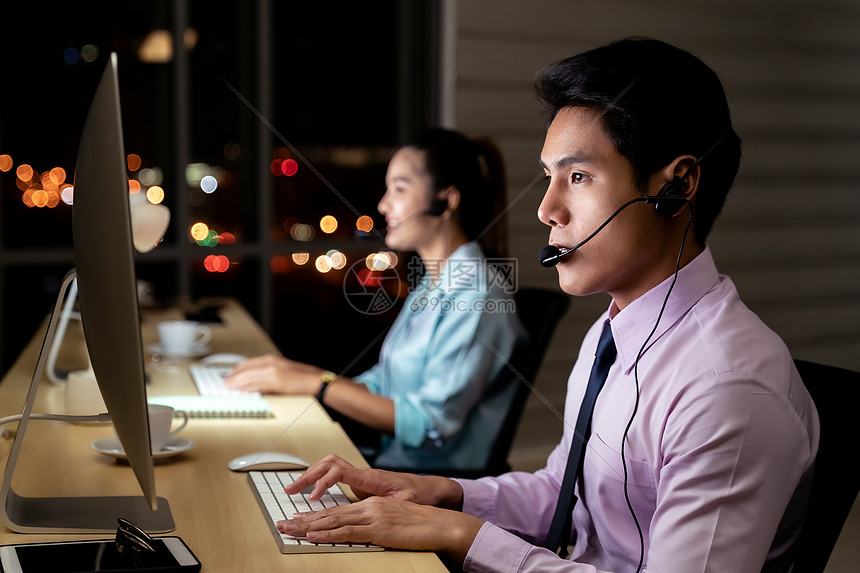 亚洲轻人信心运营商男子代理与耳机工作呼叫中心夜间环境与他的同事队客户服务技术支持用深夜努力工作24小时图片