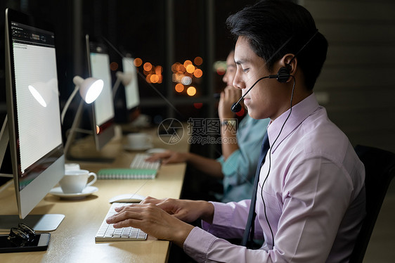 亚洲轻人信心运营商男子代理与耳机工作呼叫中心夜间环境与他的同事队客户服务技术支持用深夜努力工作24小时图片