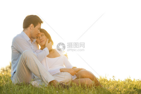 浪漫的年轻情侣坐在草地上与晴空对准天图片