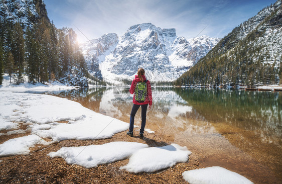女孩背着雪边的胸罩湖清水在春天阳光明媚的春天旅行与苗头女孩一起的风景水中反射山上绿树蓝天空图片