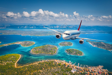 飞机在夏季阳光明媚的白天飞越小岛屿和海洋空中观察客机热带海岸有绿树天空和蓝水的山地背景图片