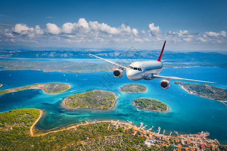 飞机在夏季阳光明媚的白天飞越小岛屿和海洋空中观察客机热带海岸有绿树天空和蓝水的山地图片