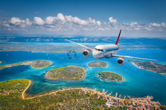 飞机在夏季阳光明媚的白天飞越小岛屿和海洋空中观察客机热带海岸有绿树天空和蓝水的山地图片