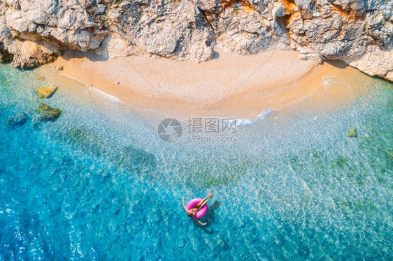 一名年轻女子与粉红甜圈游泳环在清蓝海中游泳夏季日落时有海浪沙滩和岩石热带风景与女孩凉水石头顶层风景一名年轻女子与粉红甜圈游泳环一图片