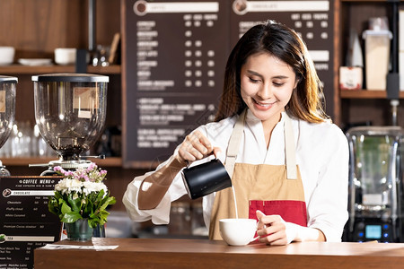 为咖啡厅的顾客准备拿铁咖啡由她的同事在背景中工作用于食品工业小型创概念图片