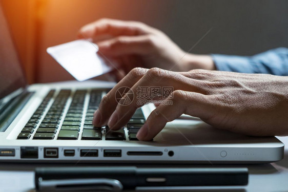 男子手持信用卡在笔记本电脑键盘上使用智能电话输入安全代码在线购物概念图片