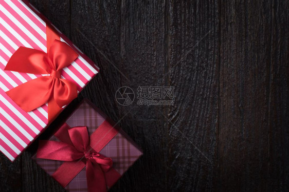一个礼物盒上面有红大彩带在旧木黑色棕褐背景上图片