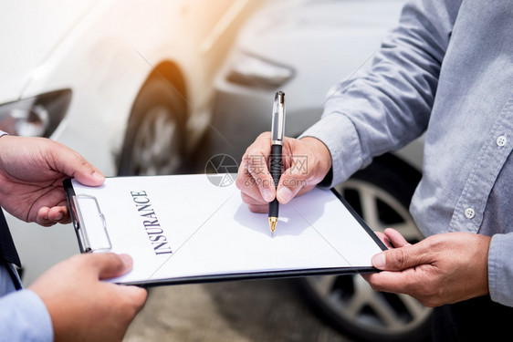 在事故后审查车辆索赔时保险代理人在剪贴板上签署保险表将笔寄给他的客户图片